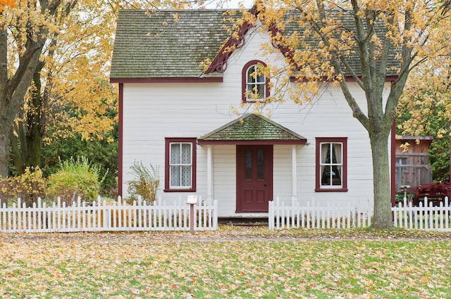 Exterior of a small white cottage with red trim during the fall